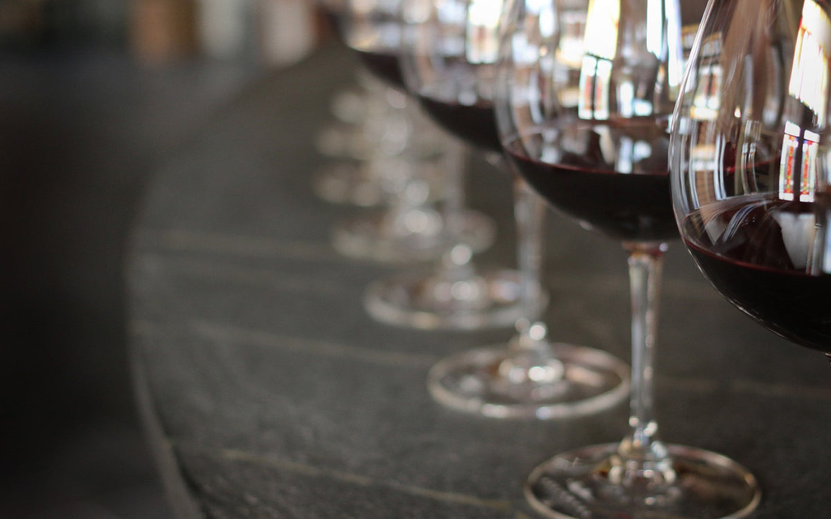 A row of wine glasses filled with red wine on a dark stone surface, photographed in soft focus.